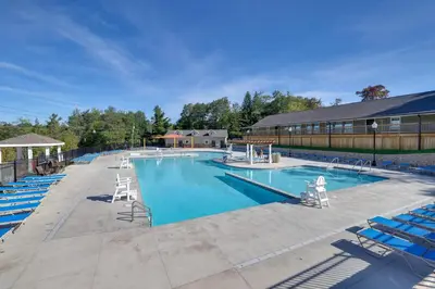 a large swimming pool with blue chairs and a building at Hot Tub and Lake Beach Access Tobyhanna Retreat! in Tobyhanna
