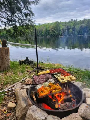 a grill with food on it next to a lake at Tentrr Riverfront Ritz in Lake Luzerne