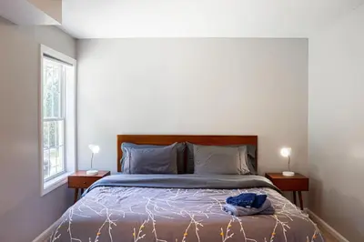 a bedroom with a bed with two nightstands and two windows at 2 Beautiful 1 BR Apartment - Central CT in Plainville