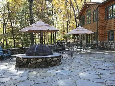 a stone patio with tables and umbrellas in front of a house at Lovely Accommodation Surrounded by Stunning Forests in Bedford near New York City in Bedford