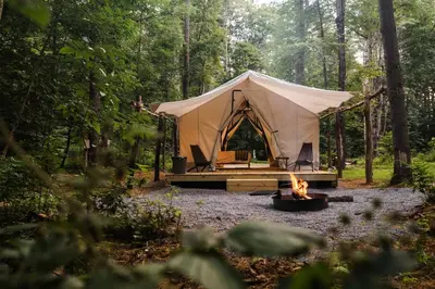 a tent in the middle of a forest with a fire at Gorgeous Safari Tent in the Lake George Area of the Adirondack Mountains, Perfect for a Family Weekend Away in Corinth