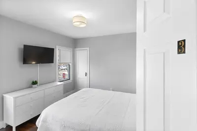 a white bedroom with a bed and a flat screen tv at Owl's Nest - 5BR apartment in New Haven