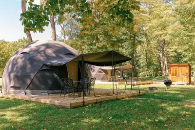 a tent with chairs and a table in a field at Boutique Glamping Dome in the Catskill Mountains in Gilboa